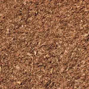 A detailed look at a large pile of Mulch reveals a textured surface made up of numerous small, irregularly shaped pieces in brown tones.