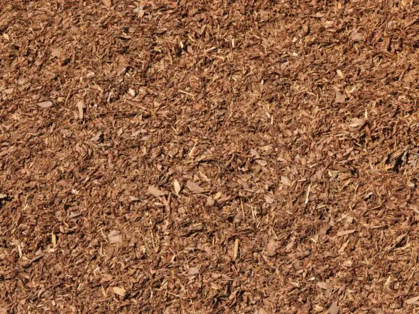 A detailed look at a large pile of Mulch reveals a textured surface made up of numerous small, irregularly shaped pieces in brown tones.