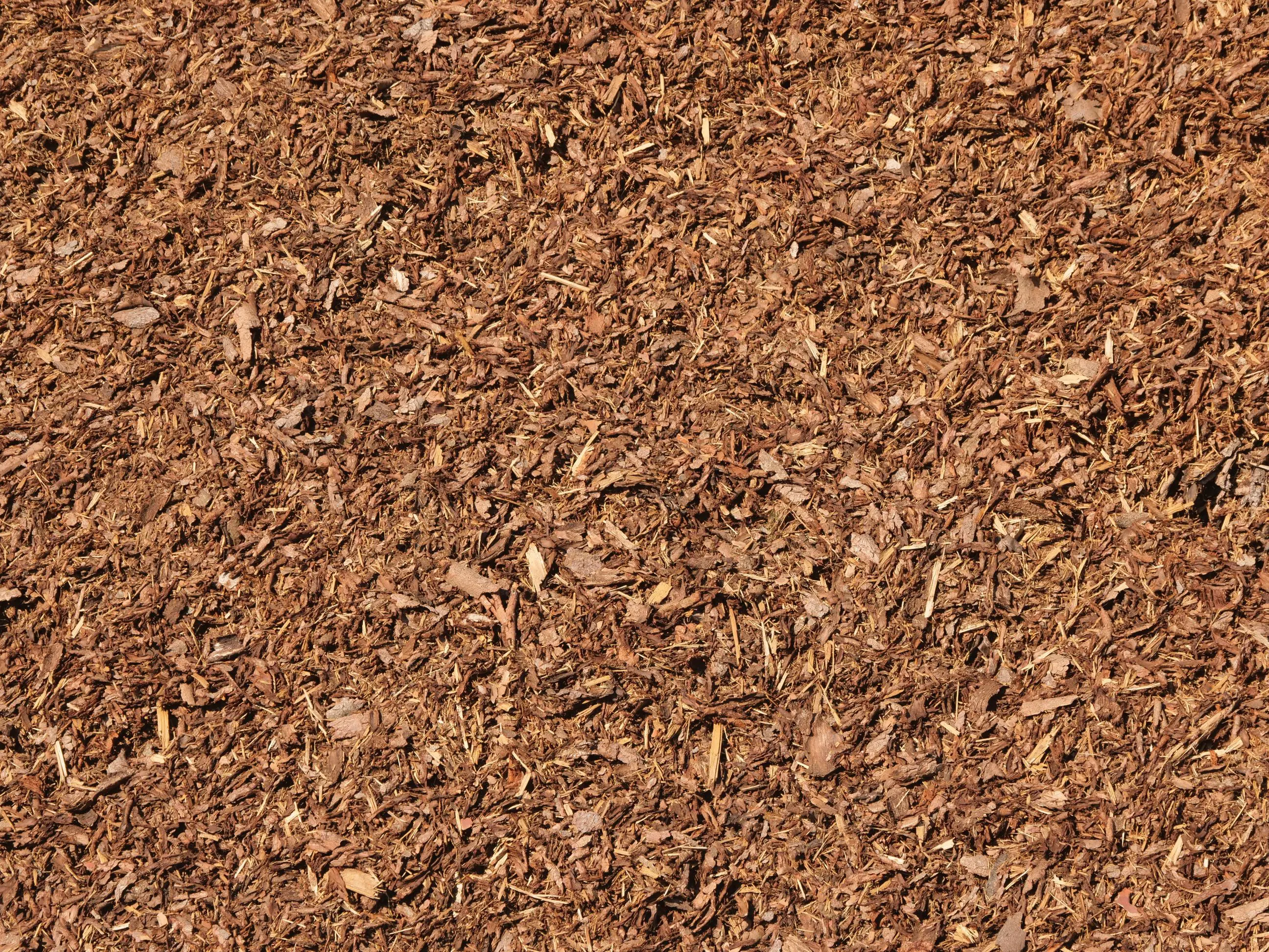 A detailed look at a large pile of Mulch reveals a textured surface made up of numerous small, irregularly shaped pieces in brown tones.