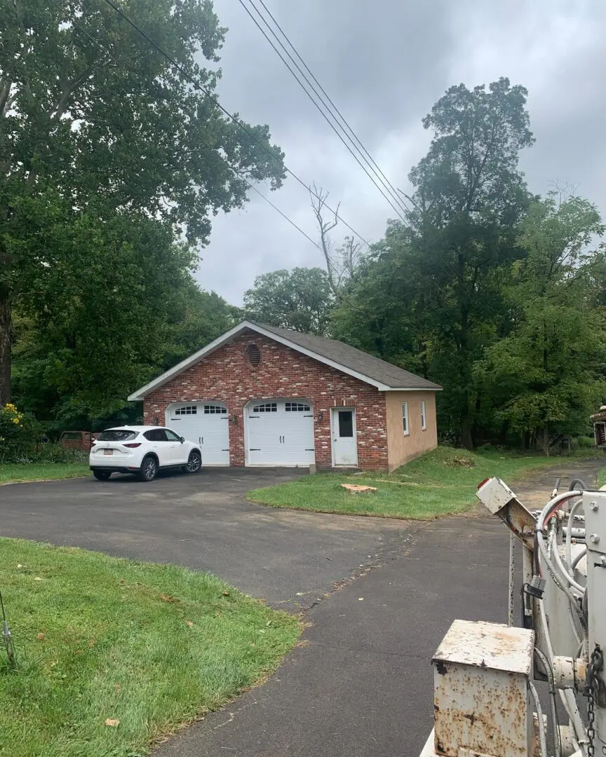 A white car parked in front of a red brick garage.