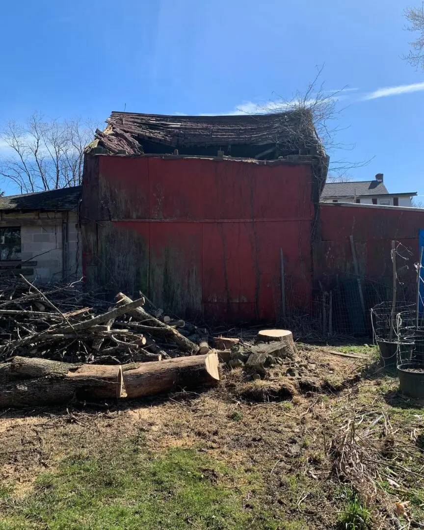 A barn with many pieces of wood in front.